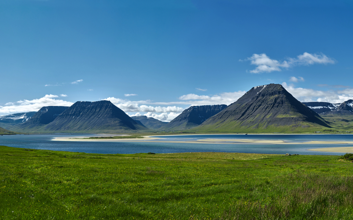Reise nach Island. Wunderschönen Sonnenaufgang über dem Meer und dem Fjord in Island. Isländische Landschaft mit Bergen,blauer Himmel und grünes Gras im Vordergrund. Blick auf die Straße zu den Häusern im Nordwesten